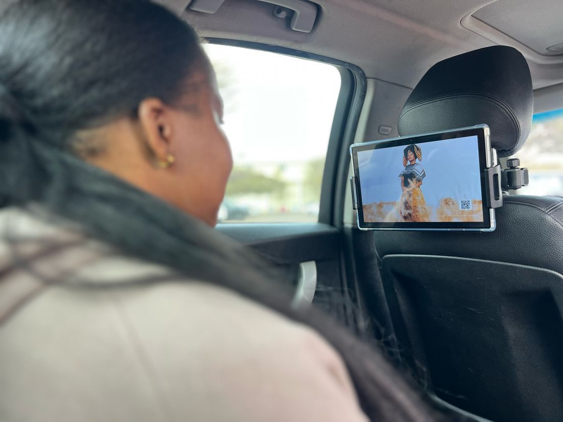 A passenger in the back of a rideshare car watching an ad on a Lumo screen mounted behind the front seat